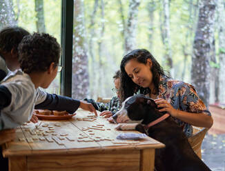 Familie mit Hund spielt Scrabble am Esstisch - CAIF32410