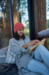 Frau entspannt sich und liest ein Buch auf der Terrasse der Hütte - CAIF32446