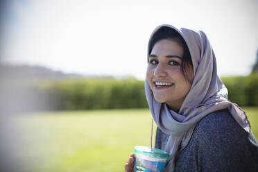Portrait happy young Muslim woman in hijab drinking juice - CAIF32457