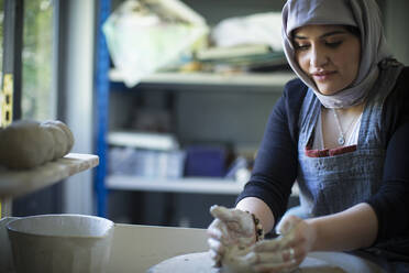 Young female Muslim artist at pottery wheel in art studio - CAIF32474