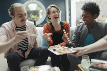 Glückliche Freunde teilen sich Sushi im Wohnzimmer - CAIF32481