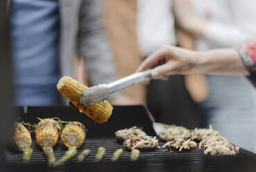 Close up woman barbecuing corn on barbecue grill - CAIF32484