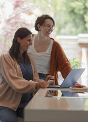 Happy women friends online shopping at laptop in kitchen - CAIF32492