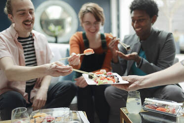 Glückliche Freunde teilen sich Sushi zum Mitnehmen im Wohnzimmer - CAIF32501