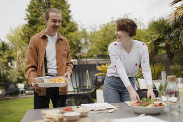 Junges Paar deckt den Terrassentisch für das Mittagessen - CAIF32510