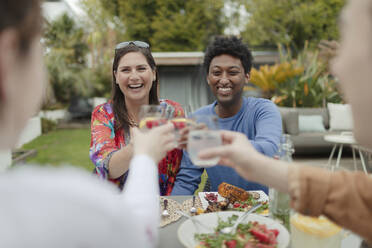 Fröhliche Freunde stoßen mit Gläsern am Terrassentisch auf das Mittagessen an - CAIF32520