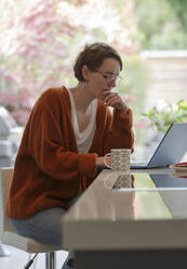 Konzentrierte junge Frau arbeitet von zu Hause aus am Laptop - CAIF32523