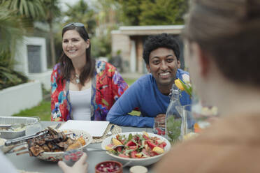 Happy couple enjoying lunch with friend at patio table - CAIF32530