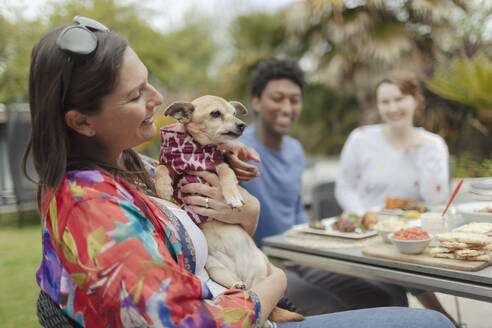 Happy woman holding cute dog at patio table - CAIF32541