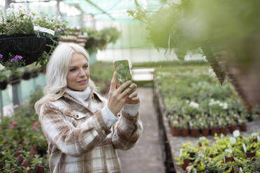 Frau mit Fotohandy, die eine Blumenampel in einem Gartengeschäft fotografiert - CAIF32550