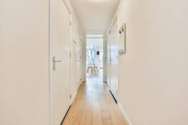 Narrow light hallway with white walls and closed room doors in stylish apartment with bright glowing lamps at home - ADSF34702