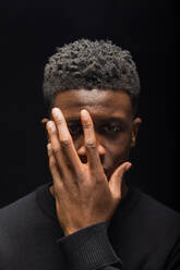 Schwarzer Mann mit kurzen lockigen Haaren, die die Hälfte des Gesichts bedecken, mit Händen auf dunklem Hintergrund im Studio - ADSF34750