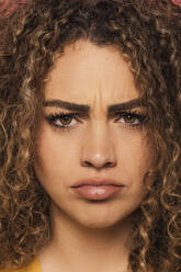 Closeup-Porträt einer jungen Frau mit lockigem Haar, die mit traurigem Gesichtsausdruck in die Kamera schaut, stehend im Studio - ADSF34763