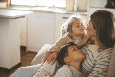 Young woman with daughter and son puckering at each other sitting on sofa - JOSEF09485