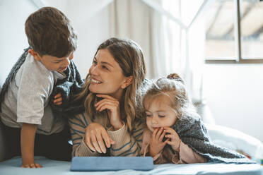 Smiling mother with son and daughter on bed at home - JOSEF09501