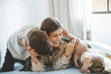 Playful mother with children lying on bed at home - JOSEF09503