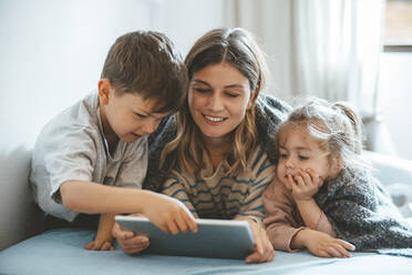 Lächelnde Mutter mit Sohn und Tochter, die auf dem Bett einen Tablet-PC benutzen - JOSEF09504