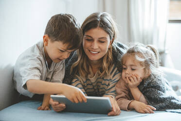 Smiling mother with son and daughter using tablet PC on bed - JOSEF09504