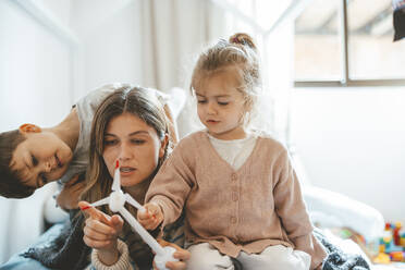 Mother holding wind turbine lying by daughter and son at home - JOSEF09507