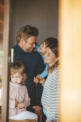 Smiling mature man spending leisure time with family in house seen through window - JOSEF09529