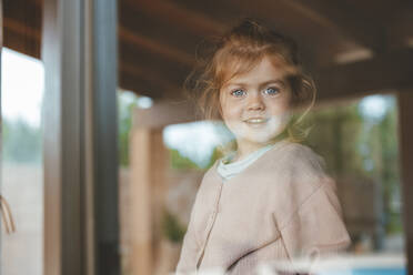 Smiling cute girl at home seen through window glass - JOSEF09532