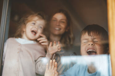Verspielter Junge drückt mit Mutter und Schwester sein Gesicht an die Fensterscheibe - JOSEF09534