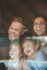 Glückliche Eltern und Kinder, die Gesichter an die Fensterscheiben drücken - JOSEF09537
