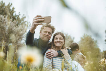 Lächelnder Mann mit Frau nimmt Selfie durch Smartphone in Wiese - JOSEF09550