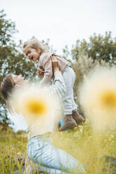 Playful young woman carrying daughter in meadow - JOSEF09556