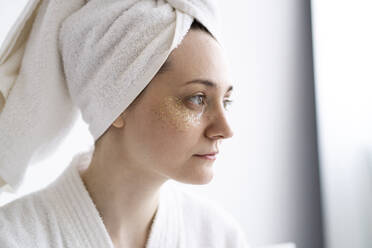 Thoughtful young woman with collagen eye mask wearing towel at home - SSGF00919