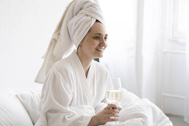 Glückliche Frau mit Handtuch auf dem Bett sitzend mit Weinglas zu Hause - SSGF00920