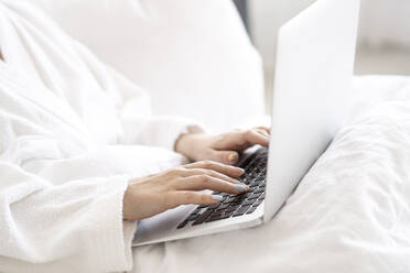 Frau mit Laptop auf dem Bett sitzend zu Hause - SSGF00922
