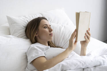 Young woman reading book on bed at home - SSGF00928