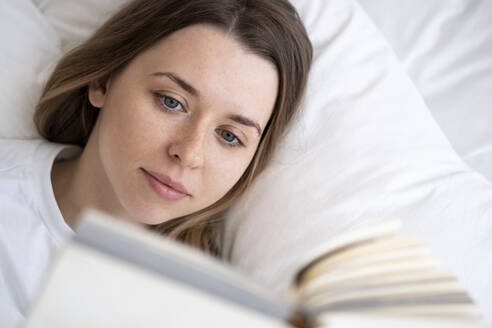 Schöne Frau, die auf dem Bett liegend zu Hause ein Buch liest - SSGF00929