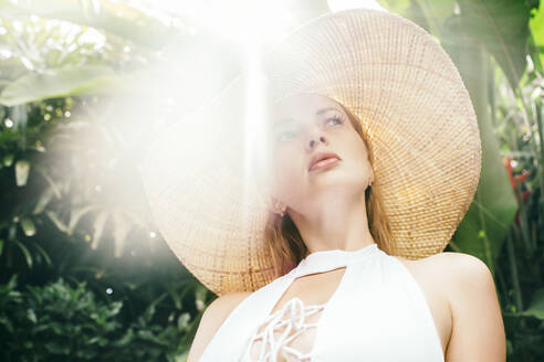 Portrait of young woman wearing straw hat illuminated by sunlight - JUBF00372