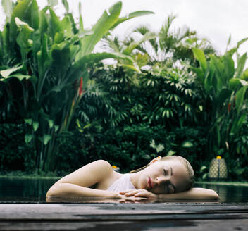 Indonesia, Bali, Portrait of young woman leaning on edge of swimming pool - JUBF00375