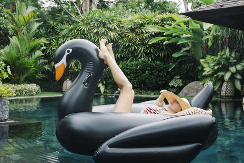Young woman relaxing on swan shaped swimming float - JUBF00377