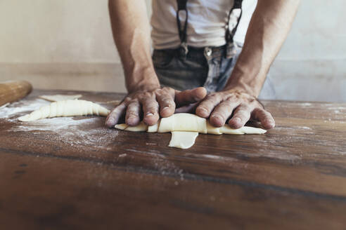 Hands of baker making croissant on table in bakery - JUBF00402