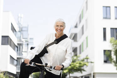 Lächelnde Geschäftsfrau mit Fahrrad vor einem Gebäude - SGF02910