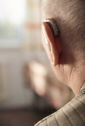 Senior man wearing hearing aid at home - AZF00405