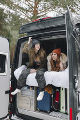 Woman talking with friend lying in campervan - MRRF02102