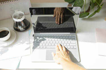 Hands of freelancer typing on laptop at desk in home office - SVKF00153