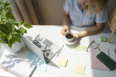 Freiberufler mit Kaffeetasse am Schreibtisch im Heimbüro sitzend - SVKF00173