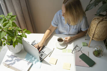 Freiberufler mit Kaffeetasse und Laptop an einem Schreibtisch im Home Office - SVKF00174