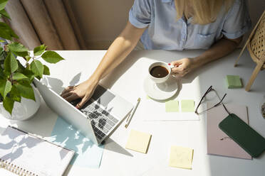 Reife Geschäftsfrau mit Kaffeetasse und Laptop am Schreibtisch im Heimbüro - SVKF00175