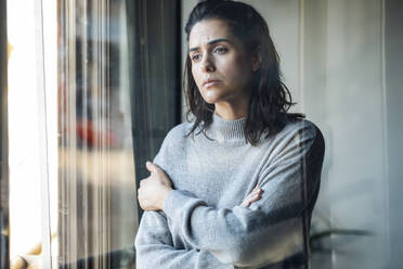 Sad woman standing with arms crossed at home - JSRF02002