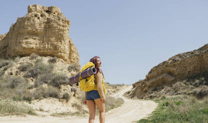 Lächelnde Frau mit Rucksack beim Wandern auf einem Feldweg - JCCMF06259