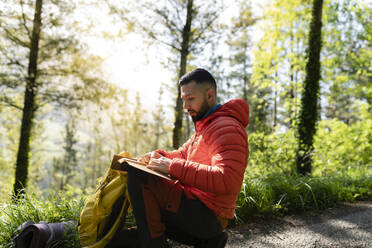 Mann liest Tagebuch im Wald sitzend - JCCMF06279