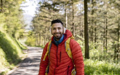 Glücklicher Mann mit drahtlosen Kopfhörern im Wald stehend - JCCMF06282