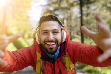 Glücklicher Wanderer, der Musik über drahtlose Kopfhörer hört und im Wald gestikuliert - JCCMF06283